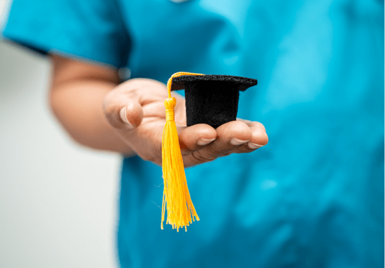 dental student in scrubs holding a mini graduation cap